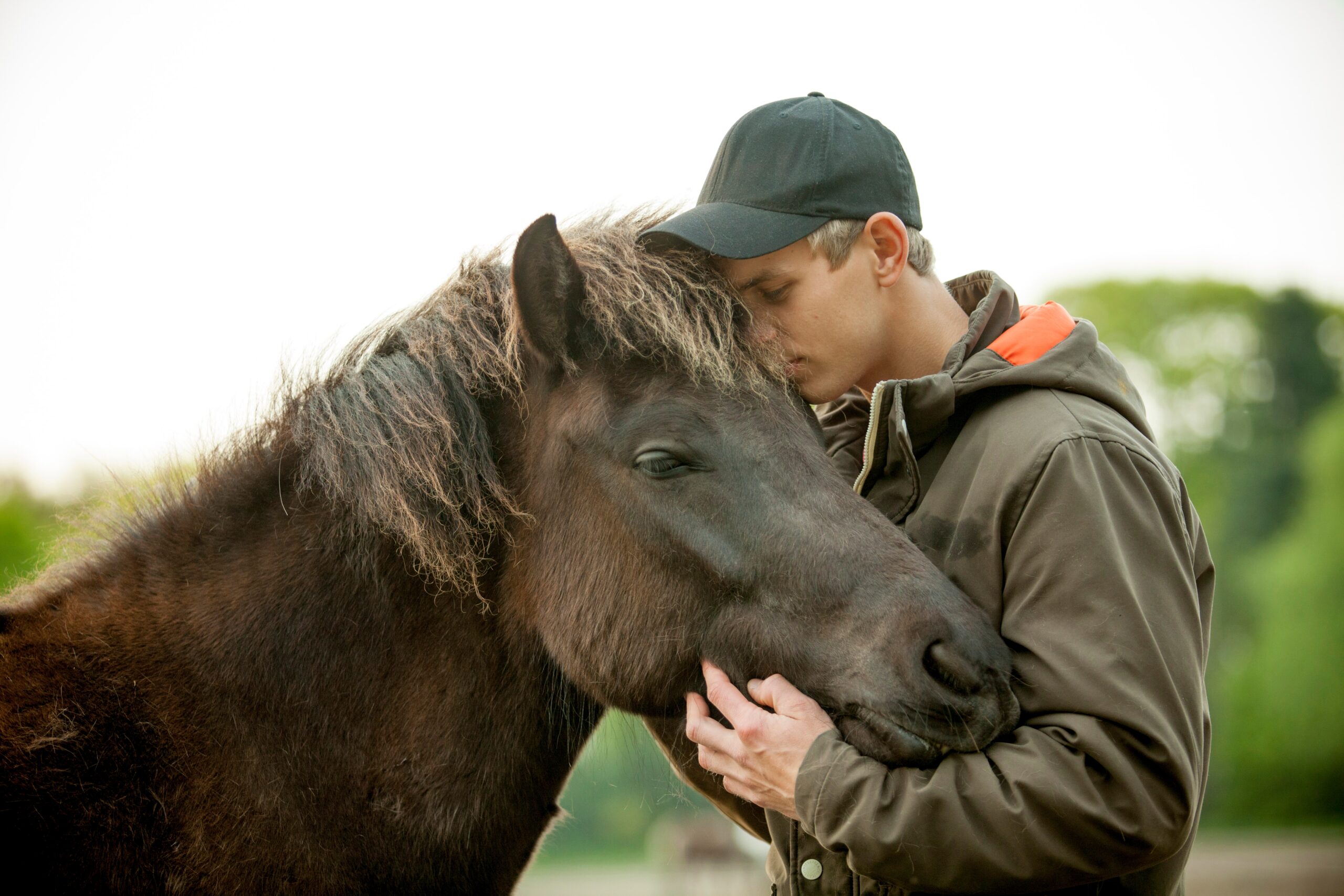 
A medium close-up shows a young man and a horse nuzzling each other